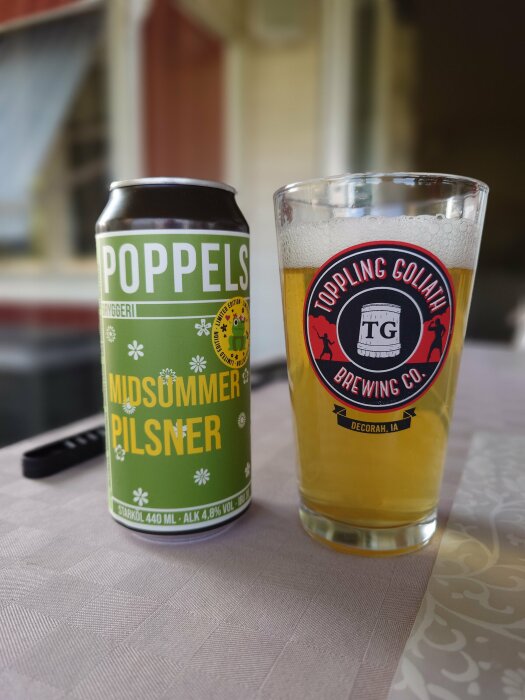 En burk Poppels Midsummer Pilsner och ett glas öl från Toppling Goliath Brewing Co. stående på ett bord.