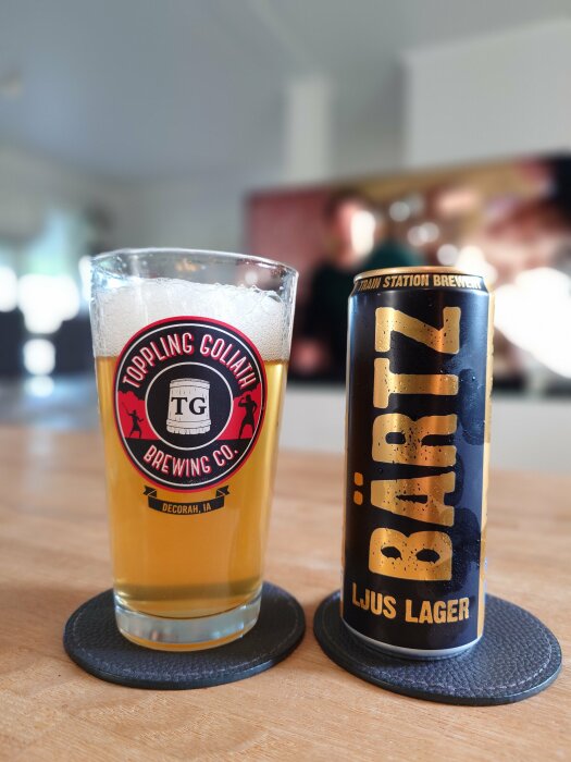 Glas med Toppling Goliath öl bredvid en burk med Bärtz ljus lager på ett bord.