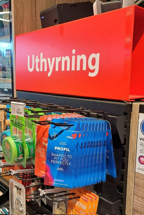 Affärshylla med skylt "Uthyrning" där det finns förpackningar med kondomer, arbetsplåster och tejp i en butik.