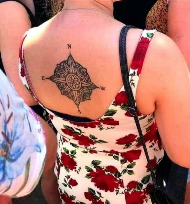 Person i blomklänning visar tatuering på ryggen föreställande en kompassros med bokstäverna N, E, S, W.