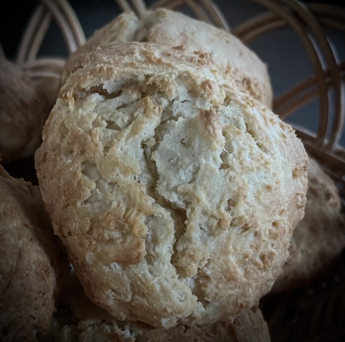 Nybakade scones fotograferade i en korg till frukost, närbild på en nygräddad scone med en gyllenbrun yta.