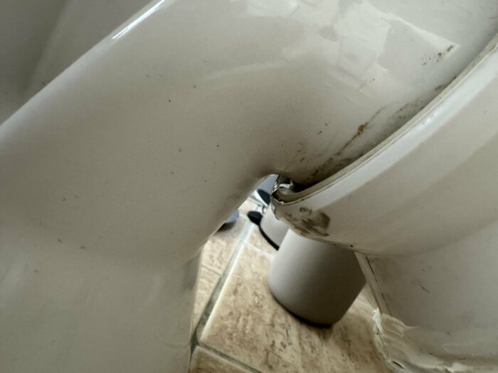 Närbild på en toalett där vatten droppar från fogarna under basen, synligt läckage.