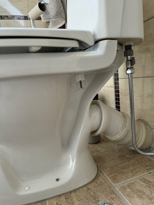 Vit toalett med synliga rörledningar och eventuellt läckage från kopplingarna på sidan.