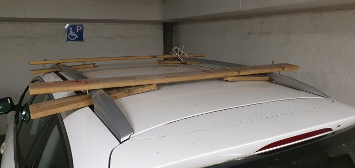 Bil med flera träplankor på takräcket, parkerad på en handikapparkering.