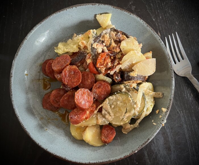 En tallrik med skivor av stekt slovakisk korv och en portion grönsaksgratäng med potatis, zucchini, tomat och aubergine.