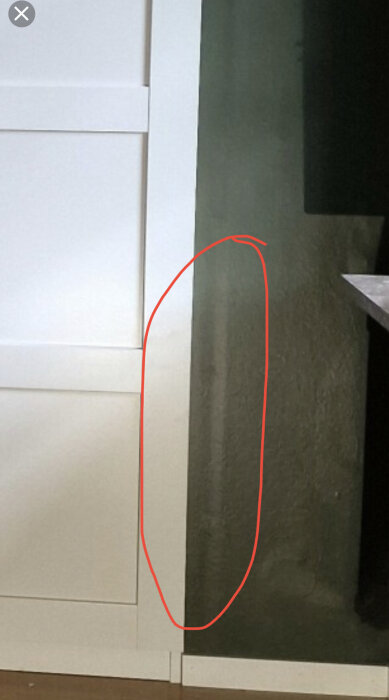 Närbild på grå vägg bredvid en vit dörrkarm, med en vertikal försänkning markerad med en röd cirkel.