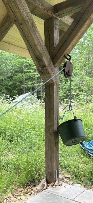 Återvunnet virke använt för konstruktion, inklusive en snickeri på en uteplats med naturbakgrund. En hink hänger från en talja fäst i trästödet.