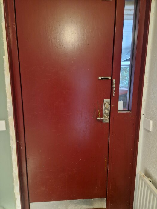 Röd dörr med små repor, mest omfattande vid dörrhandtaget.