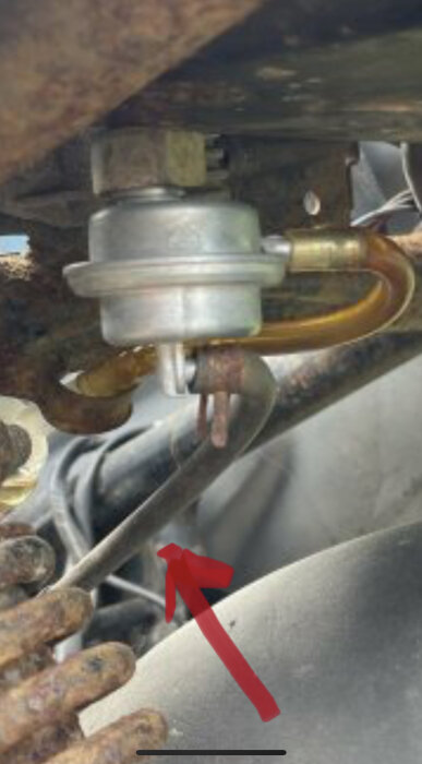 Närbild av en mekanisk komponent med anslutna rör och en svart slang, markerad med en röd pil.