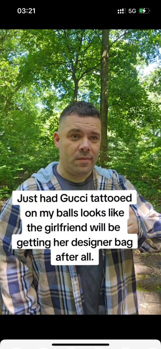 Man i skogsmiljö med kort hår och skäggstubb, iförd en rutig skjorta. Text över bilden nämner att han har tatuerat Gucci på sina pungkulor.