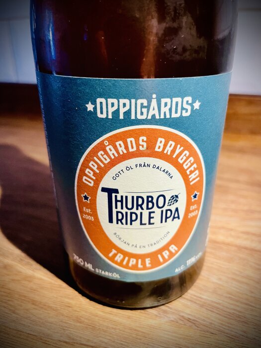 Flaska med Oppigårds Thurbo Triple IPA 750 ml starköl, etikett i blått och orange, brygd av Oppigårds Bryggeri AB.