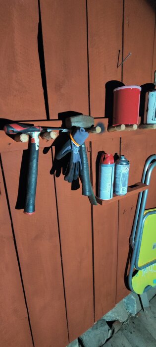 Verktyg och sprayburkar hänger på upphängningskrokar i en egen verkstad, även en arbetsbänk syns i närheten av en trävägg.