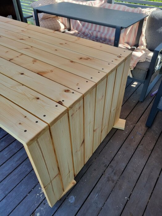 Nybyggt utebord av slätpolade träplankor med valnötspluggar och behandlat med danish oil, placerat på en altan.