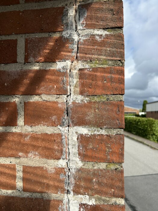 Spricka i en tegelfasad under en balkong med tidigare försök till lagning synlig. Sprickan går genom varannan tegelsten och fogen.