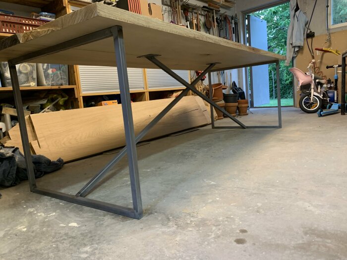 Egendesignat ekbord för uterum under bearbetning i ett garage, syns på metallben och robust träskiva. Verktyg och träplanka i bakgrunden.