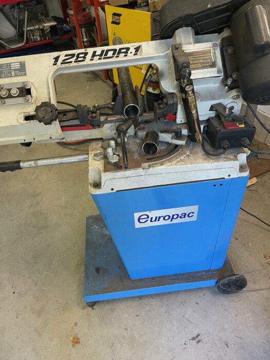 Blå Europac-maskin, modell 128 HDR.1, som används för metallarbete i ett garage med olika verktyg och utrustning i bakgrunden.