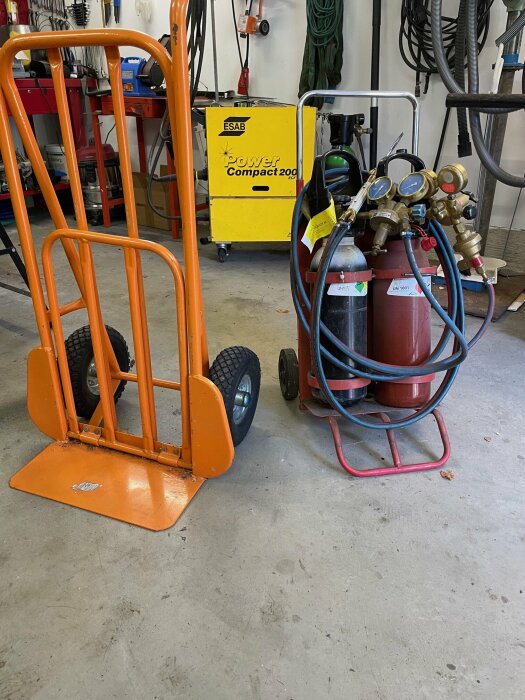 Orange pirra och gasflaskor med slangar i ett garage med en gul ESAB svetsmaskin i bakgrunden.