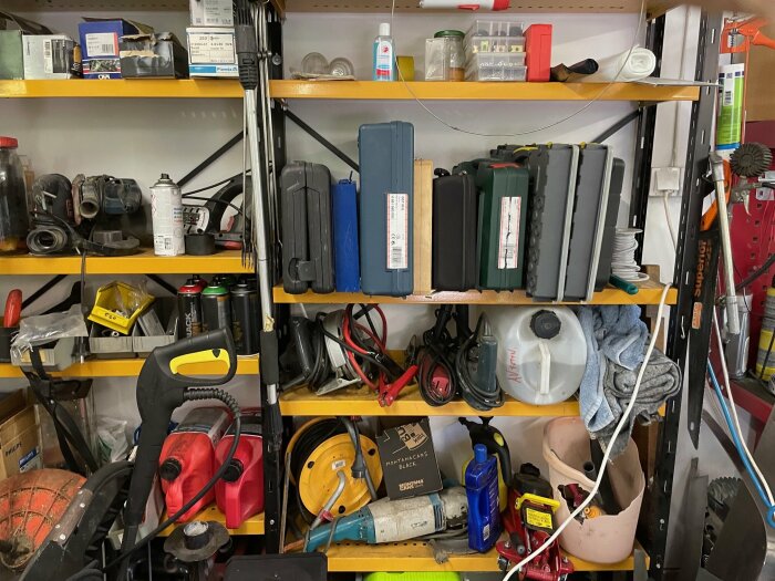 Garagehyllor fyllda med olika verktyg och maskiner till salu, inklusive borrmaskiner, slangar, sprayflaskor, plastdunkar och verktygslådor.