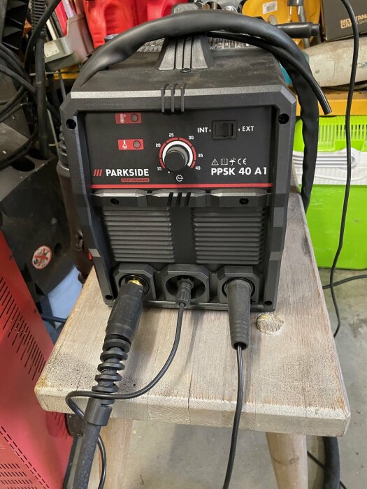 Svetsmaskin av märket Parkside PPSK 40 A1, placerad på en träbänk i ett garage, med kablar och andra verktyg synliga i bakgrunden.