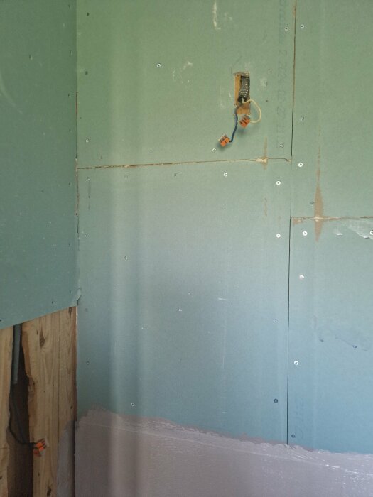 Grönt gipsvägg i ett badrum under renovering med synliga elektriska kablar och anslutningar vid en öppning i väggen.