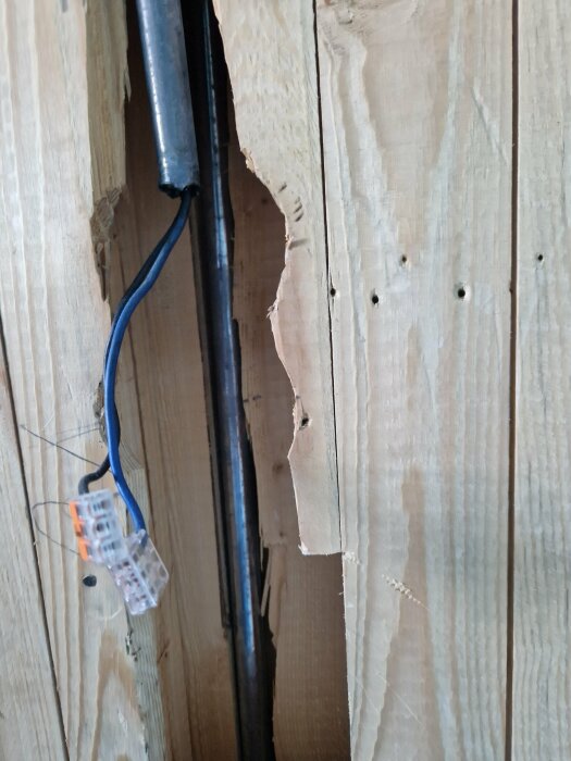 Blå kabel ansluten via kopplingsplint bakom träpanel i en sommarstuga.