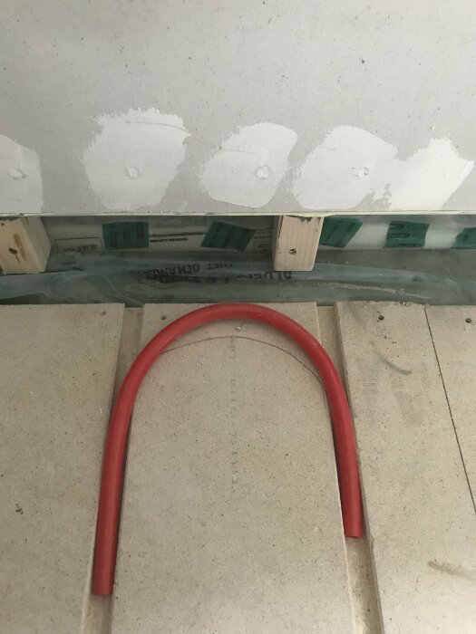 Golv med glapp mellan golv och vägg, röd kabel liggandes i ett spår längs golvet mot väggen fixad med gipsskivor.