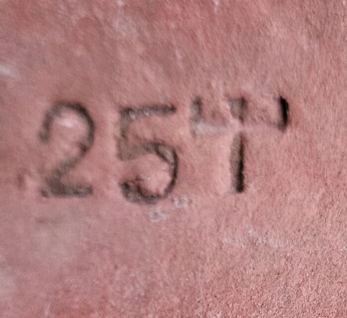 Stämpel på rött tegel med texten "257" och en symbol som liknar ett "T" med tre hakar uppåt.