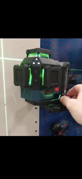 Bosch Professional GLL 330-80 CG 18V-laser med gröna lysdioder justeras på en pegboard. Verktyget är märkt med bluetooth och batteriindikatorer.