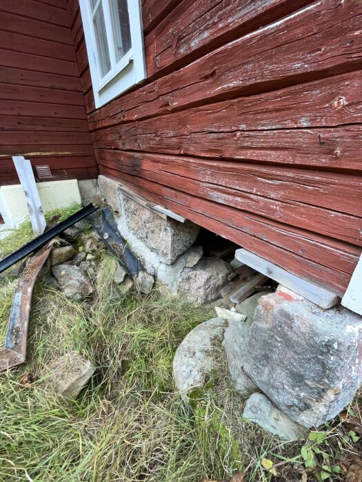 Husets hörn med synliga stenar vid dess grund, där marken har satt sig vilket orsakat en spricka i fasaden. Gräs och lösa stenar syns runtomkring.