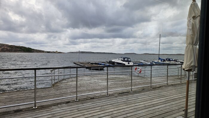 Utsikt över en småbåtshamn från en restaurang i Lysekil, med flera båtar förtöjda vid bryggan och kuperade öar i bakgrunden under en molnig himmel.