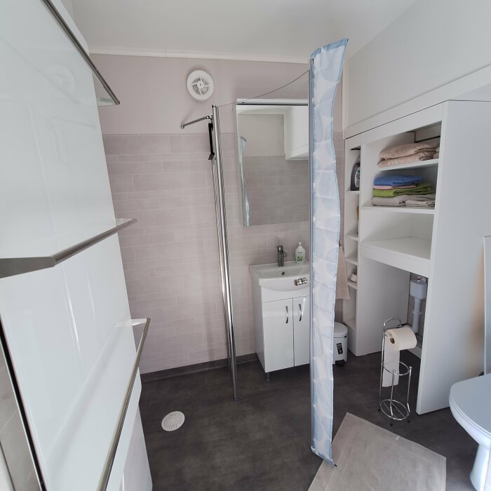 Ett nyrenoverat badrum med handfat, spegel, duschvägg och öppen förvaring med hyllor fyllda med handdukar. Duschväggen är installerad och modifierad.