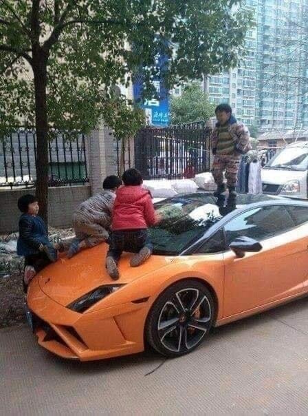 Barn leker och hoppar på en orange Lamborghini parkerad på en gata i en stad.