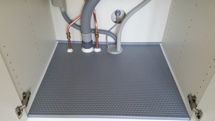 Vattensäker köksunderskåp med grå skyddsmatta och korrekt monterade kopparrör samt avloppsrör.