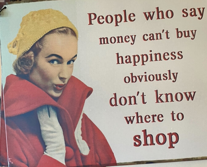 Kvinna i röd kappa och gul mössa, med texten "People who say money can’t buy happiness obviously don’t know where to shop" bredvid henne.