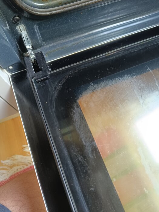 Närbild på vänstra hörnet av en öppen ugnsugn, med fokus på listen runt glaset där det syns matrester och smuts. Ugnen är av märket Ikea.
