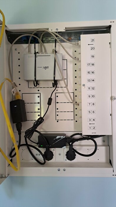 Fiberomvandlare, router och nummermärkt patchpanel i ett öppet Garo nätverksskåp med inkopplade nätverkskablar och strömkontakter.