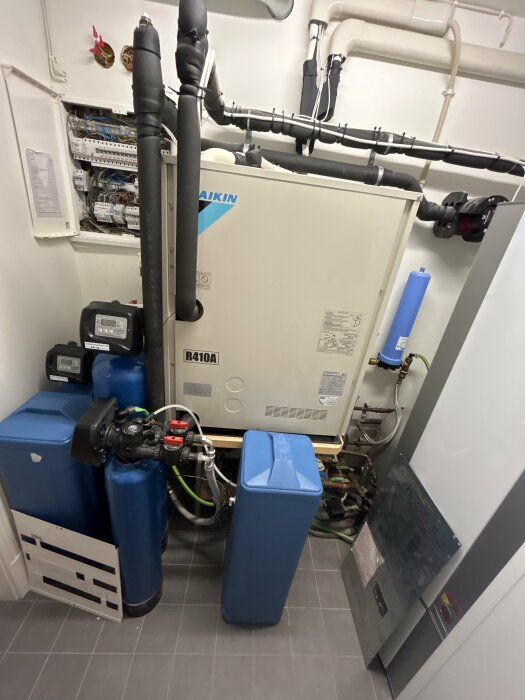 Teknikrum med en stor värmepump från Daikin, blå vattentankar, rör och ventilationssystem.