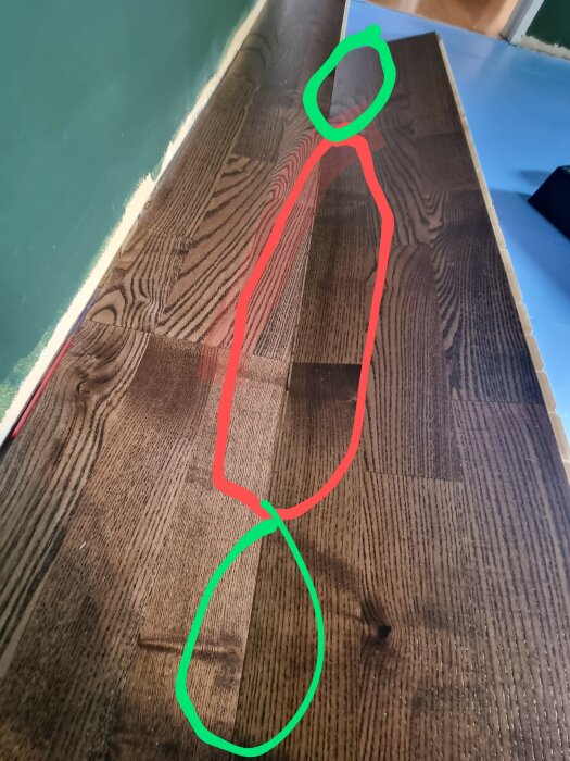 Närbild på ett mörkt trägolv där plankorna inte passar perfekt. De markerade gröna områdena visar plankornas ändar som passar, medan det röda området visar mitten där de inte når ihop.