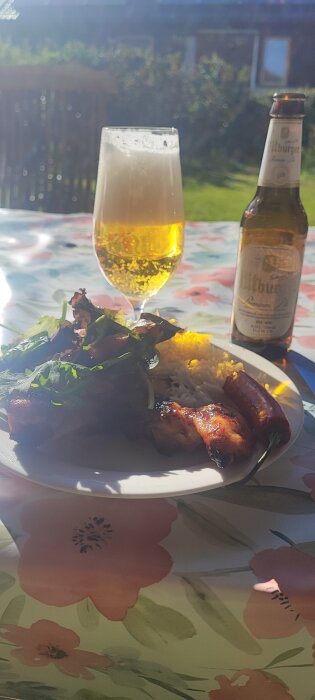 Grillade kycklingvingar med Basmati ris, en röd peppar, grön sallad och ett glas öl står på ett bord utomhus. En ölflaska syns i bakgrunden.
