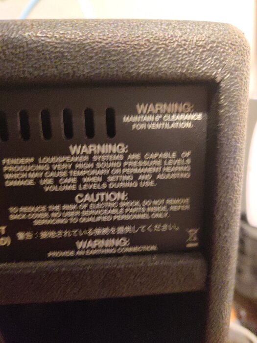 Oskarp bild av baksidan på en förstärkare med varningstexter och symboler för ventilation och jordning.