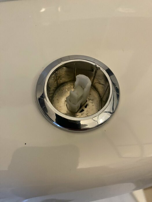 Spolknappen på en toalett, saknar yttre knapp, endast innerdelen synlig i en förkromad ram.