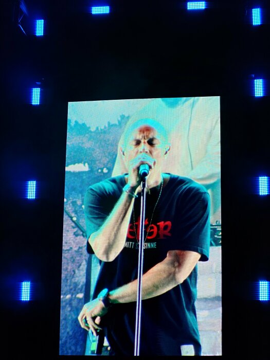 En person sjunger i en mikrofon på en scen med blåa scenljus i bakgrunden.