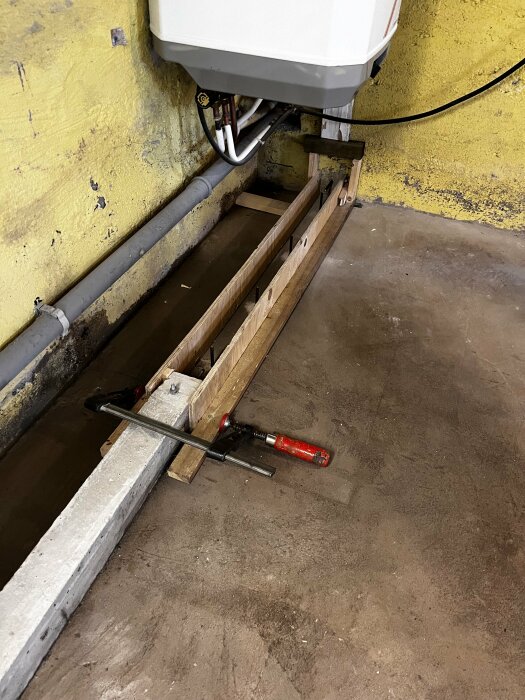 Formsättning och verktyg i källaren för att gjuta en klack till en innervägg. Väggarna är gulmålade och diverse rör är installerade.