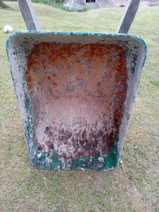 Rostig skottkärra med avskavd färg, placerad på en gräsmatta.