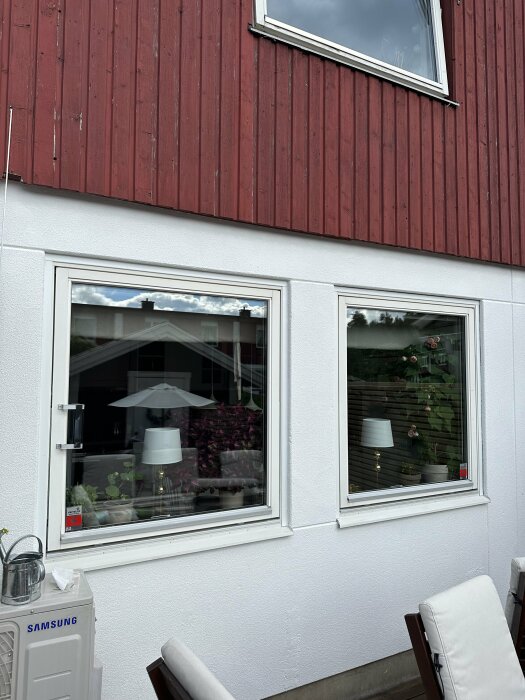 Fasad av ett radhus med vit lättbetong och röd träpanel. Fönster och utemöbler syns samt en luftvärmepump från Samsung på väggen. Uteplats i förgrunden.