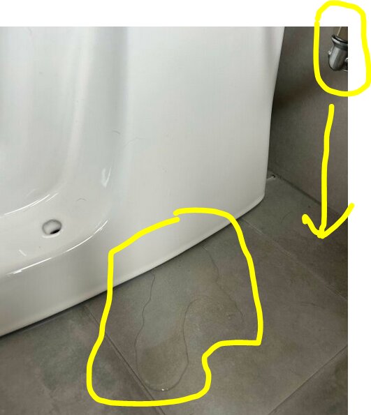Vattenpöl på golvet bredvid botten av en vit toalett med anslutande rör som visas med gul markering.