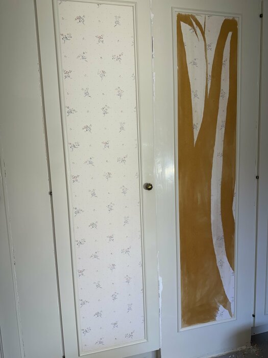 Två garderobsdörrar, en med vit bakgrund och blommönster och en med delvis borttagen blommig tapet och påbörjad spackling, synliga sprickor vid väggen.