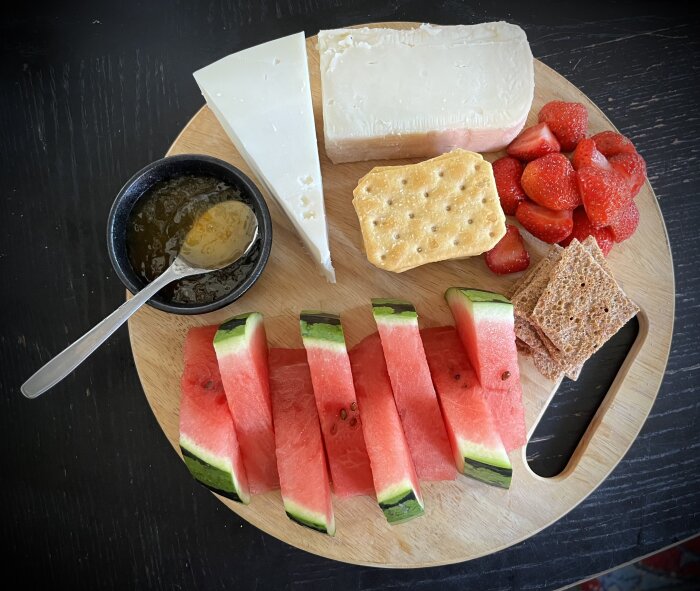 Ostbricka med vattenmelon, jordgubbar, olika sorters ost, kex, rågknäckebröd och honung på ett runt träfat.