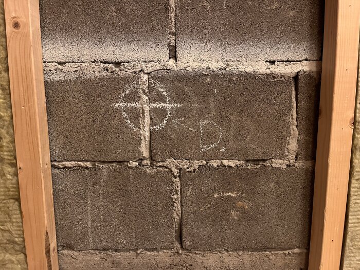 Markeringar på betongvägg med ett kors, bokstaven "D" och en pil. Träram runt väggen på sidorna.