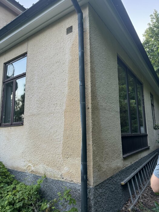 Fuktfläckar och missfärgningar på en vit fasad, framför en hängränna och stuprör, i ett gammalt hus efter flera dagar med regn.